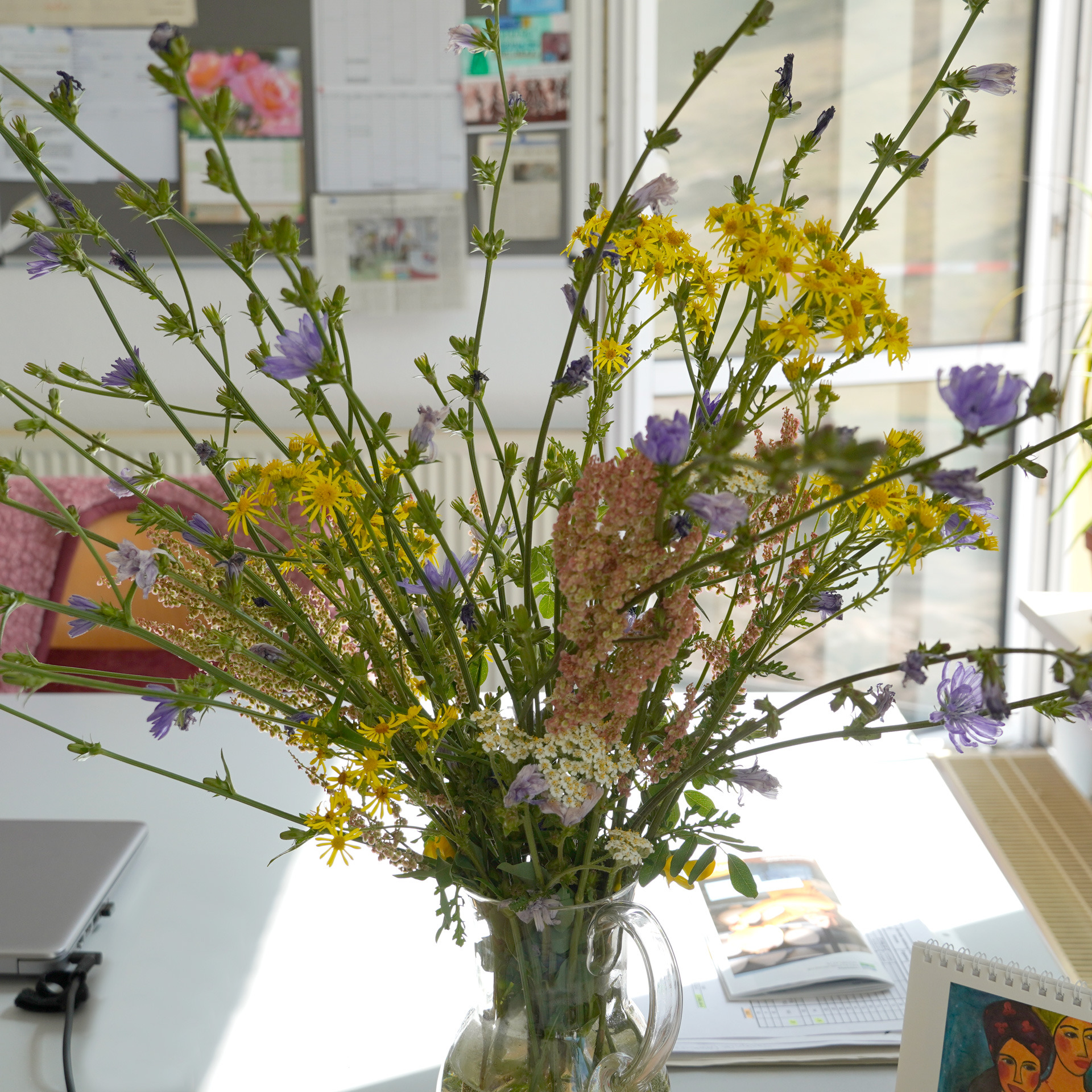 Kornblumen in einer Vase auf dem Schreibtisch mit offenen Fenster im Hintergrund